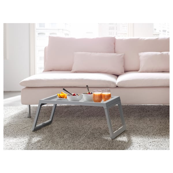 Modern bed tray on a couch with bowls, glasses, and fruit, ideal for meals and snacks.