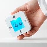 Hand holding a KLOCKIS device, displaying digital alarm clock with time 10:10.