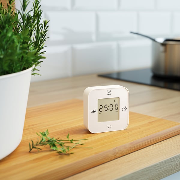 White alarm clock displaying 25:00 on wooden table, beside a plant and rosemary.