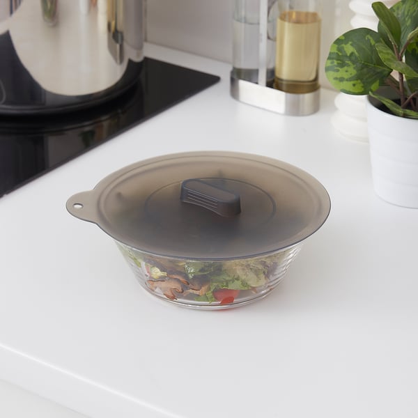 KLOCKREN lid in black silicone on glass bowl with ingredients, sitting on a white kitchen counter. Bowl is small, near a kettle and a plant.
