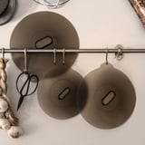 Three brown silicone lids hang from a metal bar with hooks, designed for various pots and pans, featuring a vacuum seal and versatile kitchen use.