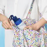 A person holding a colorful KNALLA umbrella with a protective cover and strap.