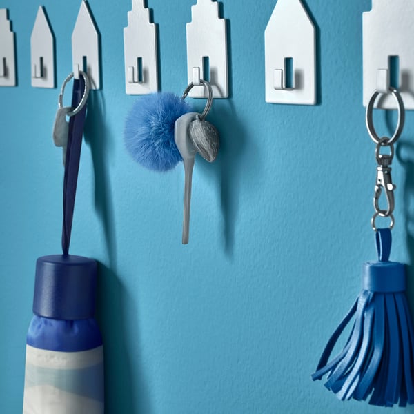 Keys hang on wall hooks, some with blue bottle, keychain with blue pom-pom and tassel.