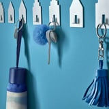 Keys hang on wall hooks, some with blue bottle, keychain with blue pom-pom and tassel.