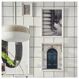 Three framed black-and-white photos on a white tiled wall show a door, stairs, and road. Left, a white hanging lamp and plant.