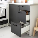 Modern kitchen cabinet with three drawers open, showing utensil storage. Grey and white with black handles, designed for practical space use.