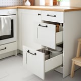 White kitchen cabinet with three open drawers, one holding a metal bin. KNOXHULT organizer for easy access to items.