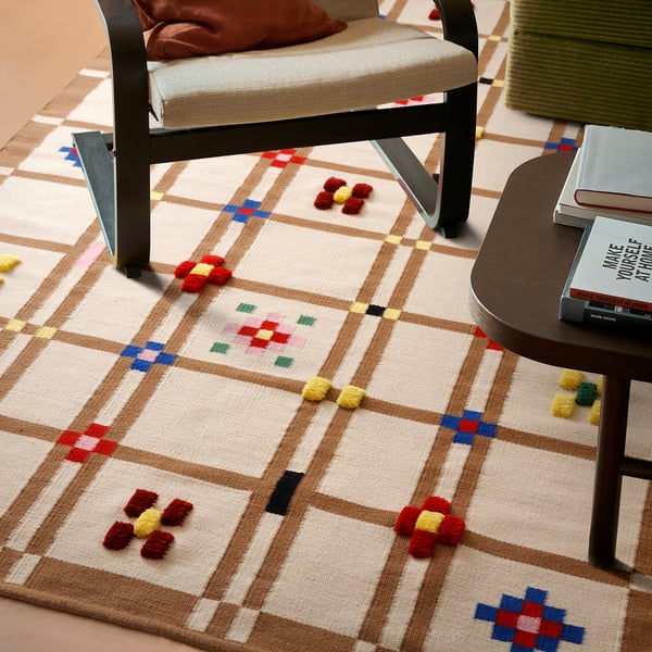 Colorful woven rug with pom-poms, chairs, and books on side table, ideal for comfort and style.