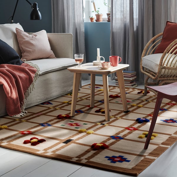 Living room with KNYLHAVREN wool rug. Beige, multicolored, rectangular, fits under sofa and wicker chair.
