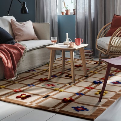 Living room with KNYLHAVREN wool rug. Beige, multicolored, rectangular, fits under sofa and wicker chair.