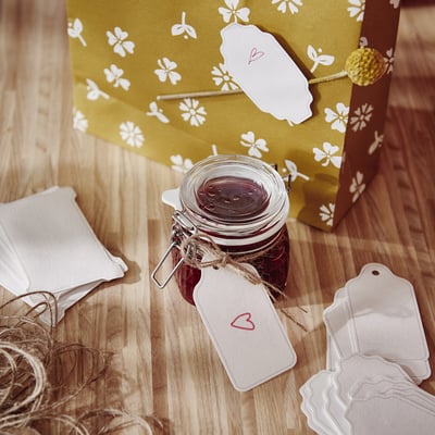 Jar with dark contents beside yellow gift bag, heart tag, jute, on wood.
