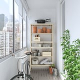 Balcony with white KOLBJÖRN storage unit holding pots, pans, and kitchen items. A bike and plant beside it, with city view from window.