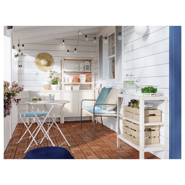 Bright balcony with wooden floor, white furniture, blue cushions, plants, and string lights.