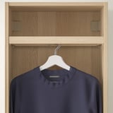 A wooden closet unit with a hanging rail displaying a navy blue garment on a white hanger.