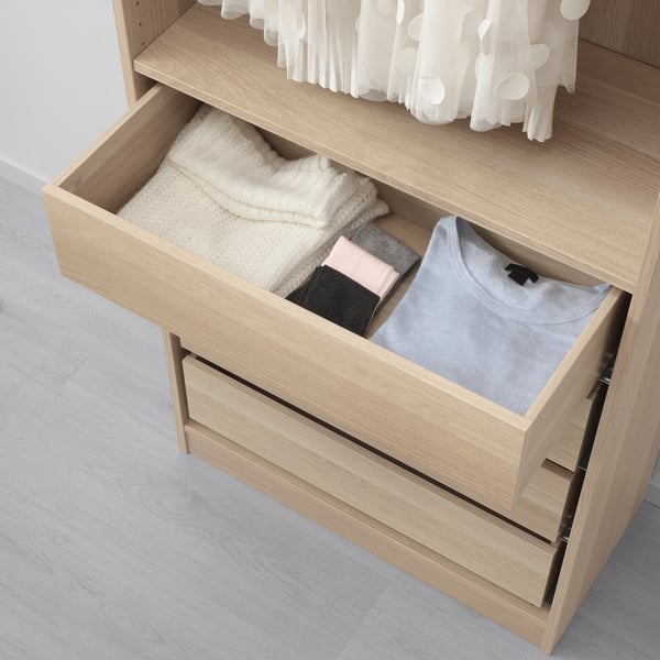 A wooden dresser drawer, partially open, filled with neatly folded clothes including t-shirts, socks, and underwear, demonstrating organized storage.