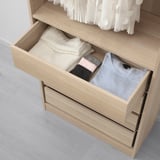 A wooden dresser drawer, partially open, filled with neatly folded clothes including t-shirts, socks, and underwear, demonstrating organized storage.