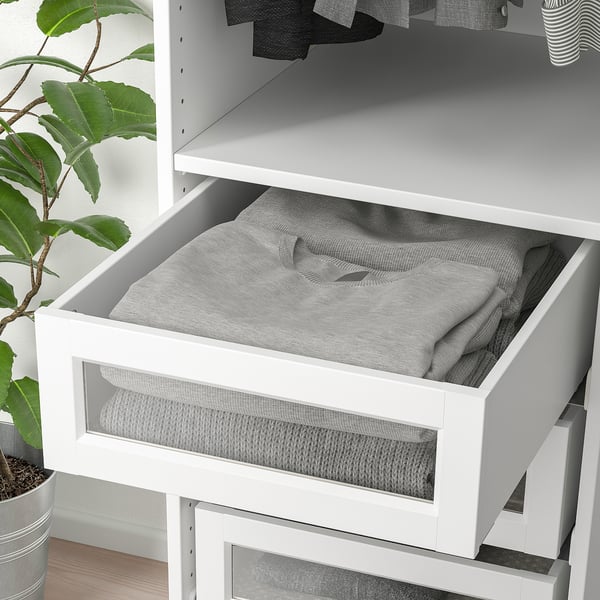 A white wardrobe drawer with glass front, holding folded gray clothes, part of a pax system.