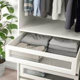 A white system wardrobe with clear glass drawers neatly folded gray clothes.