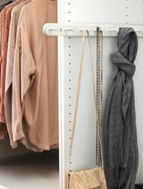 A closet with beige blouses, grey scarves, and accessories organized on KOMPLEMENT white hangers and shelves.