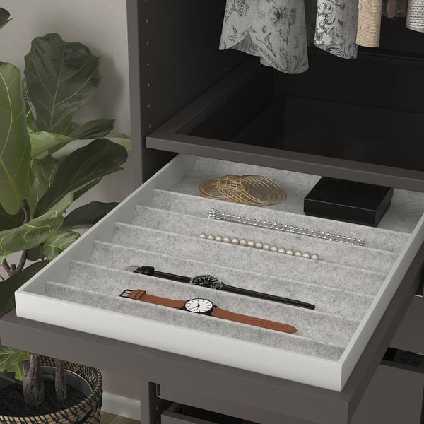 Open jewelry tray with watches, pearls, & bracelets in sections, beside a plant.