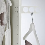 A valet hanger on a closet wall, holding an empty coat hanger, designed for airing or preparing clothes.