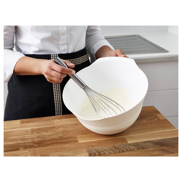 A person whisking cream in a white bowl on a wooden countertop, demonstrating the use of the KONCIS whisk.