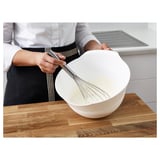 A person whisking cream in a white bowl on a wooden countertop, demonstrating the use of the KONCIS whisk.