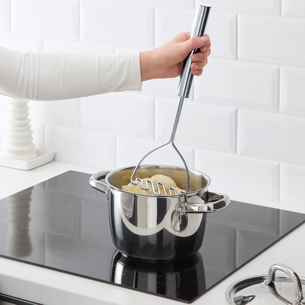 Person is using a KONCIS potato masher on a stove. The masher has a long handle for easy reach into pots, creating smooth vegetable mash.
