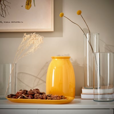 Yellow ceramic dish on white counter with decor, vases, and books. Botanical art in background.