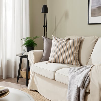 Cozy living room with beige striped cushions, neutral combo on white couch, floor lamp, side table, and plant nearby.