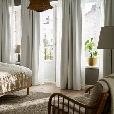 Bright bedroom with large KORGMOTT white block-out curtains, a cozy bed, and a wooden chair by a wide window.