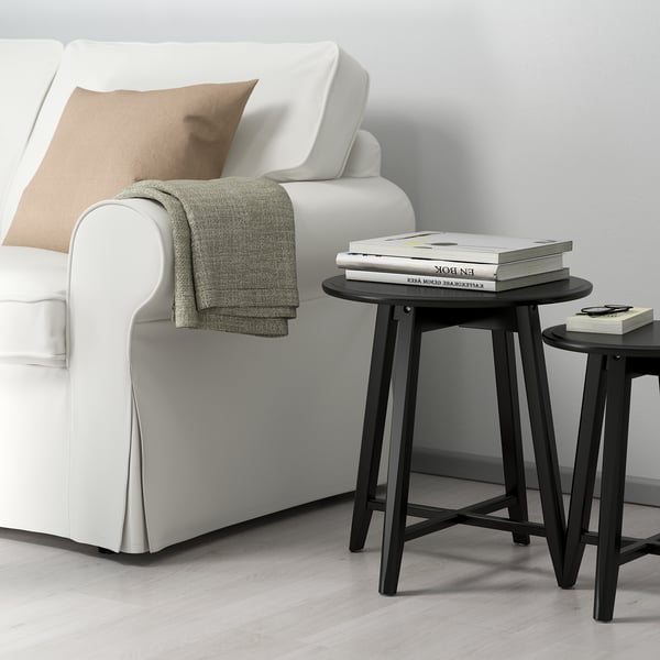 Black KRAGSTA nesting tables with soft shapes. Perfect for space-efficient, stylish living room decor next to a large sofa.