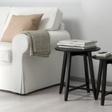 Black KRAGSTA nesting tables with soft shapes. Perfect for space-efficient, stylish living room decor next to a large sofa.