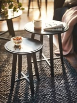 Two round black nesting tables with white cup, snacks, and magazines. Soft, modern design with metal legs.