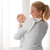 A woman holds a baby in a white KRAMA cloth. The cloth protects her shoulder, showcasing its absorbent and practical use.