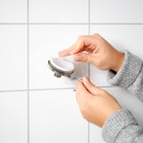 Person attaches KROKFJORDEN white suction hook to tiled wall.