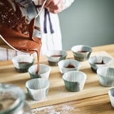 Person pouring batter into cupcake liners on wooden board.