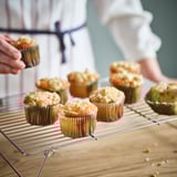 Person placing fresh muffins on a cooling rack. Muffins are in paper baking cups.