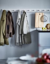 White KUBBIS coat rack with hooks, scarves, jackets. Kitchen counter with cutting board, strainer, fruits.