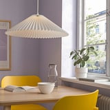 White lamp over wooden table with yellow chairs, plant, purple walls.