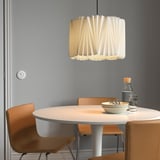 Modern dining area with round KUNGSHULT beige lamp, wooden chairs, tabletop items, and grey wall.