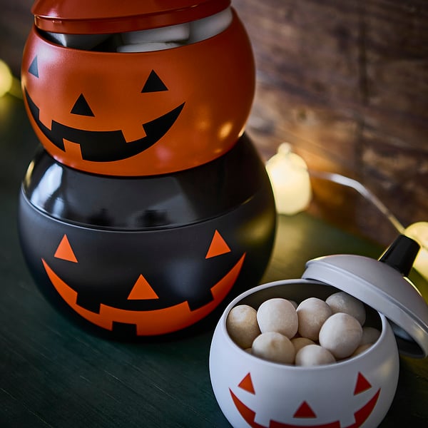 Three halloween-themed jack-o-lantern containers, stacked and filled with candies, on a table.