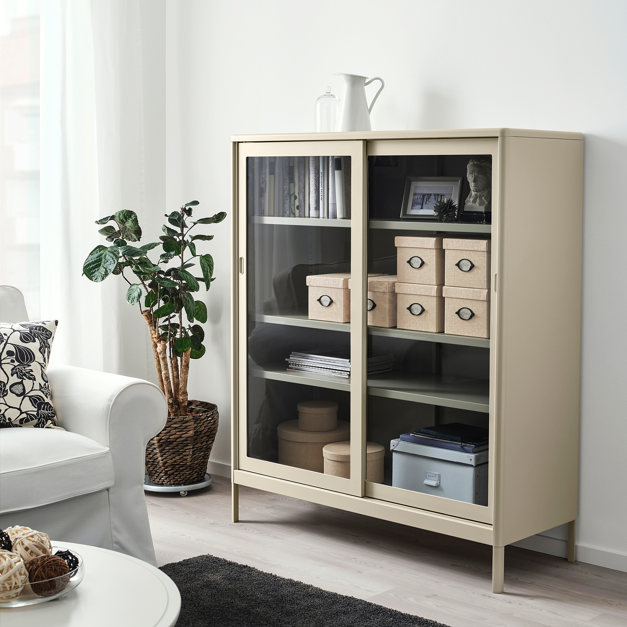 A KVARNVIK light beige cabinet with glass doors, organized shelves, and a plant beside a white chair.