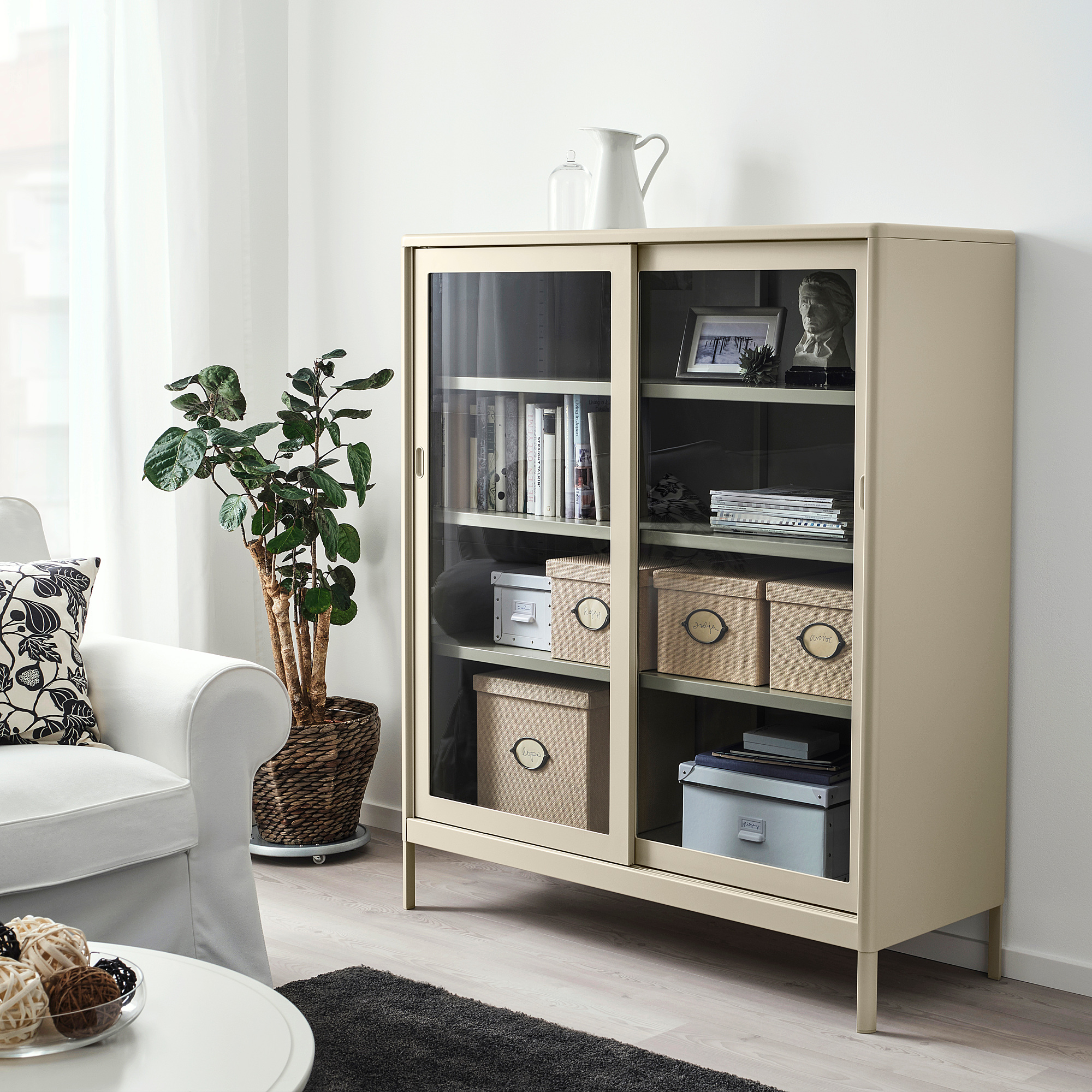 KVARNVIK glass-door storage cabinet with books and decor, next to a chair and plant.