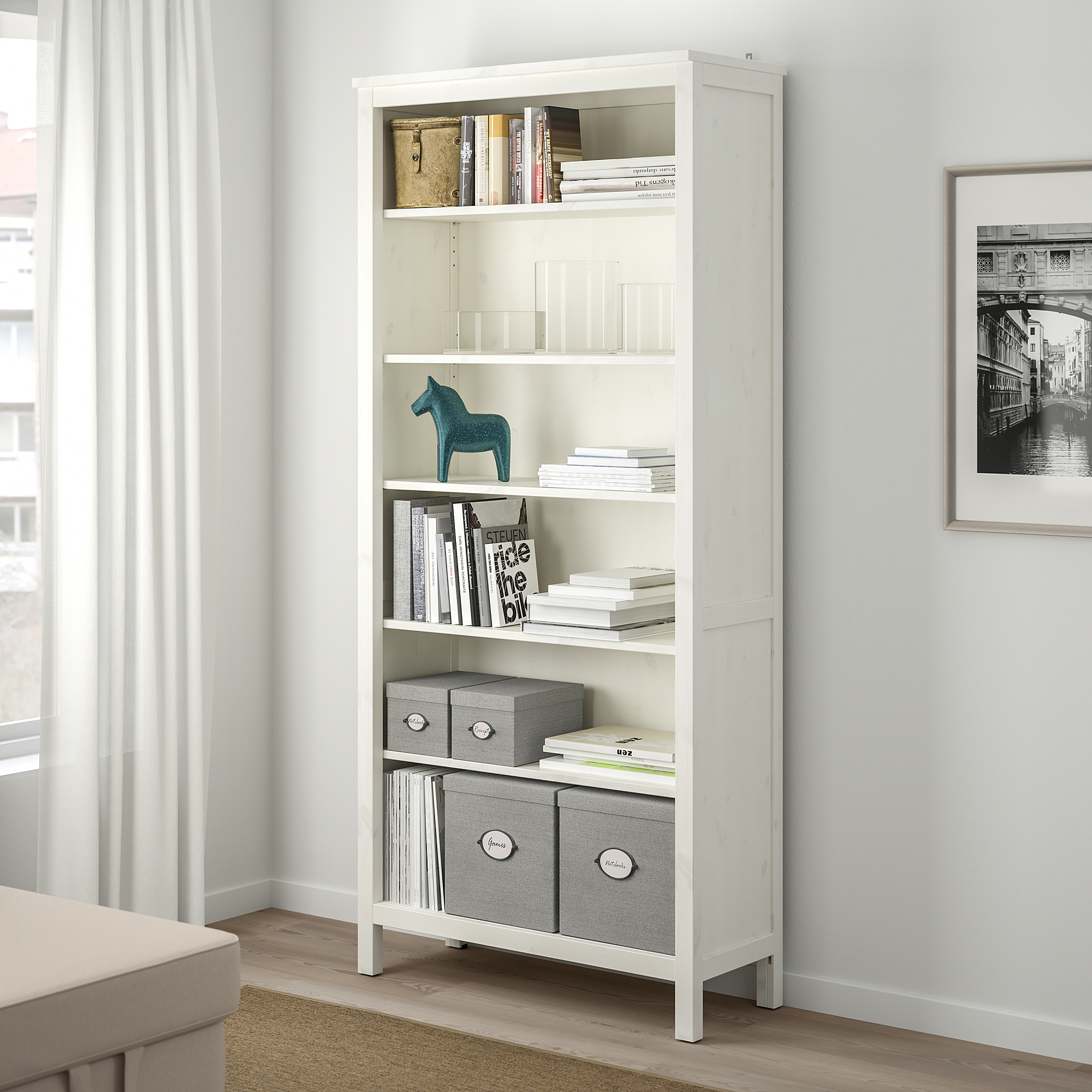 White KVARNVIK shelf unit under window, holding books, boxes, and decor.