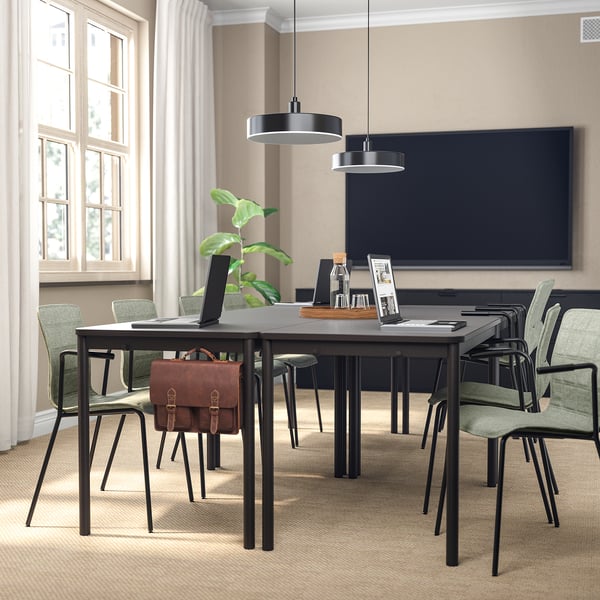 Minimalist conference room with LÄKTARE chairs, dark table, green fabric, screen, plant, laptop, briefcase, natural light.