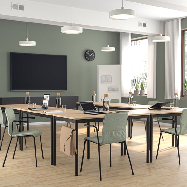 Modern office with wooden tables, green chairs, large screen, and natural light.