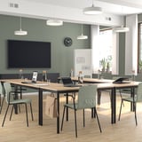 Modern office with wooden tables, green chairs, large screen, and natural light.