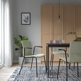 Modern dining area with four green LÄKTARE chairs around a small black table. Four cabinets, a plant, and a framed picture decorate the room.