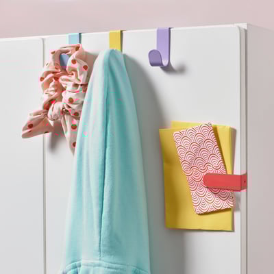 Colorful LÄTTHET hooks hang a towel, scarf, and hold notes on a door.